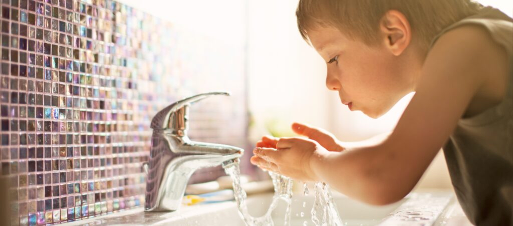 Ett barn dricker vatten direkt från vattenkranen.